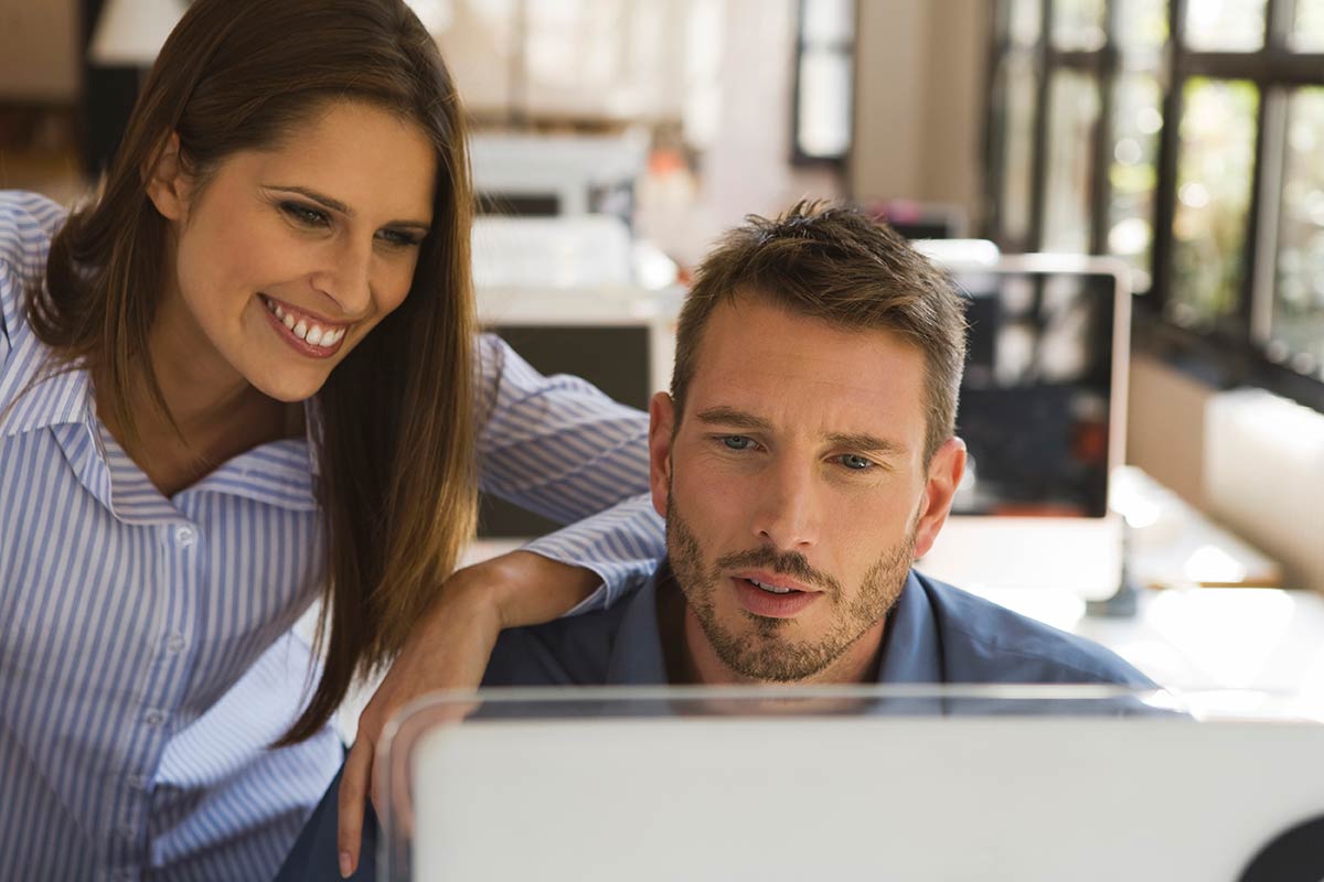 Zwei Mitarbeiter schauen auf den Bildschirm. Sie prüfen die Vertriebszahlen in Dynamics 365 Sales.