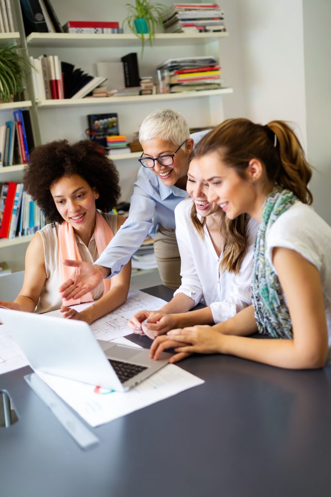 Gruppe 4er glücklicher Kolleginnen, die gemeinsam an am Schreibtisch beraten
